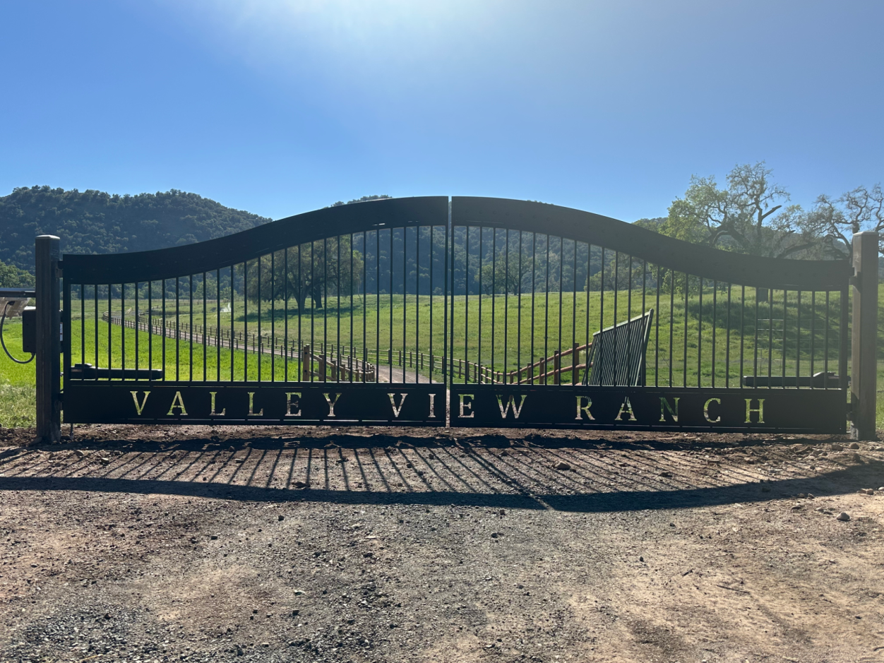 Black gated entrance to Valley View Ranch, surrounded by green fields and hills.