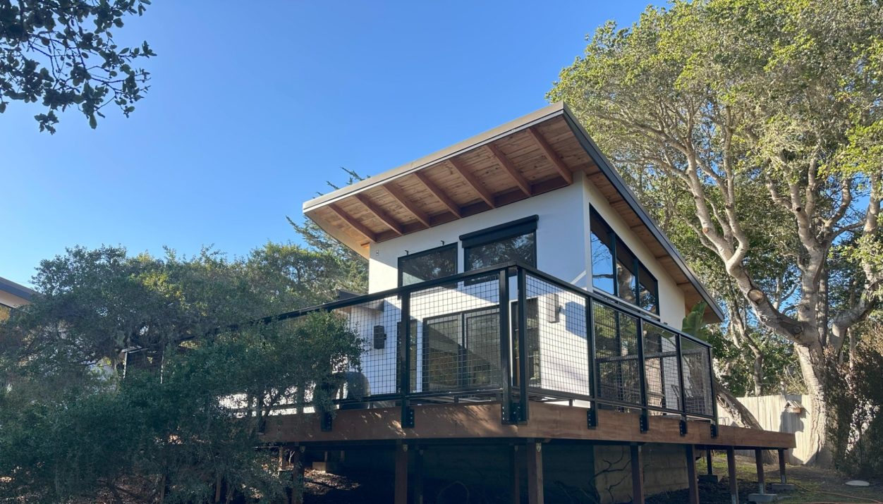 Modern house on a raised deck surrounded by trees and clear blue sky.