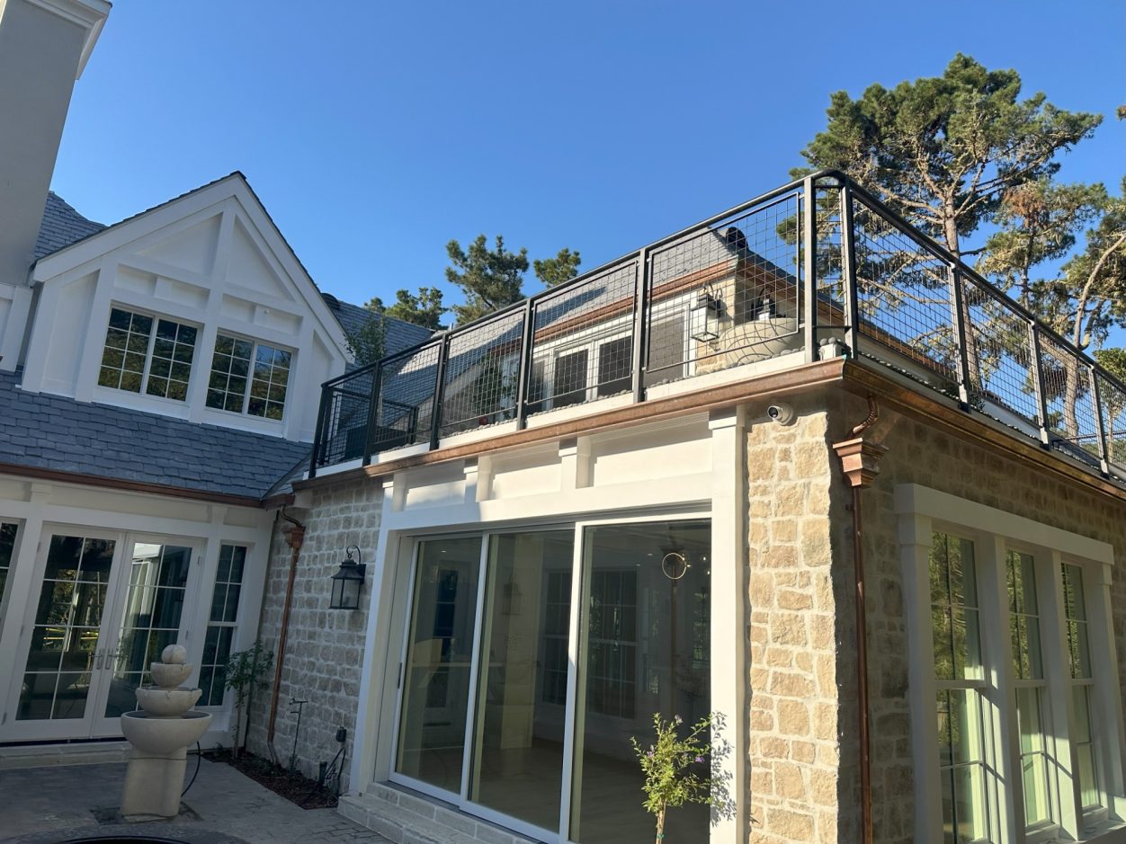A modern house exterior with a balcony and large windows under a clear blue sky.