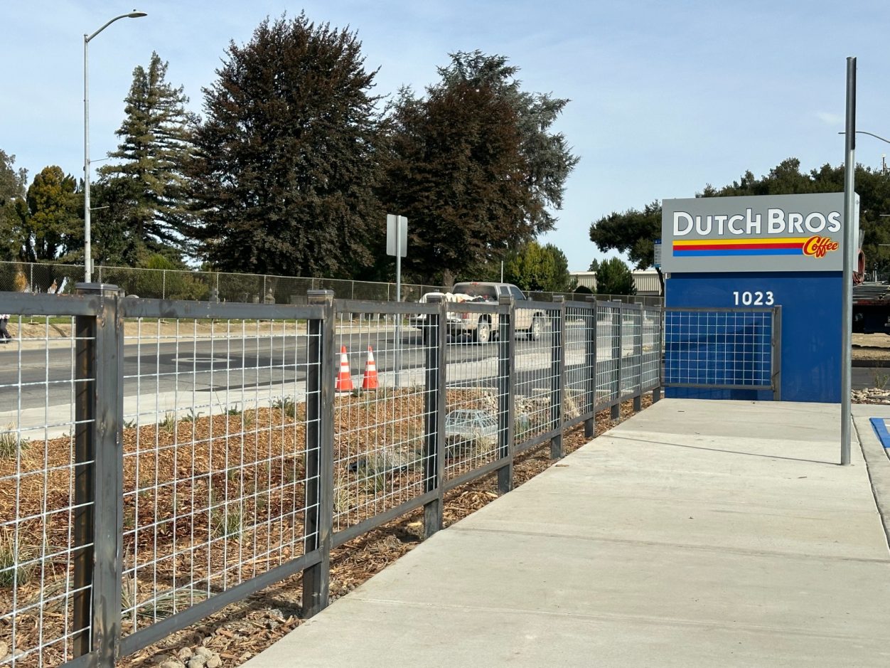 Barriers and sidewalk near a Quick Bros location, with trees and construction signage in the background.