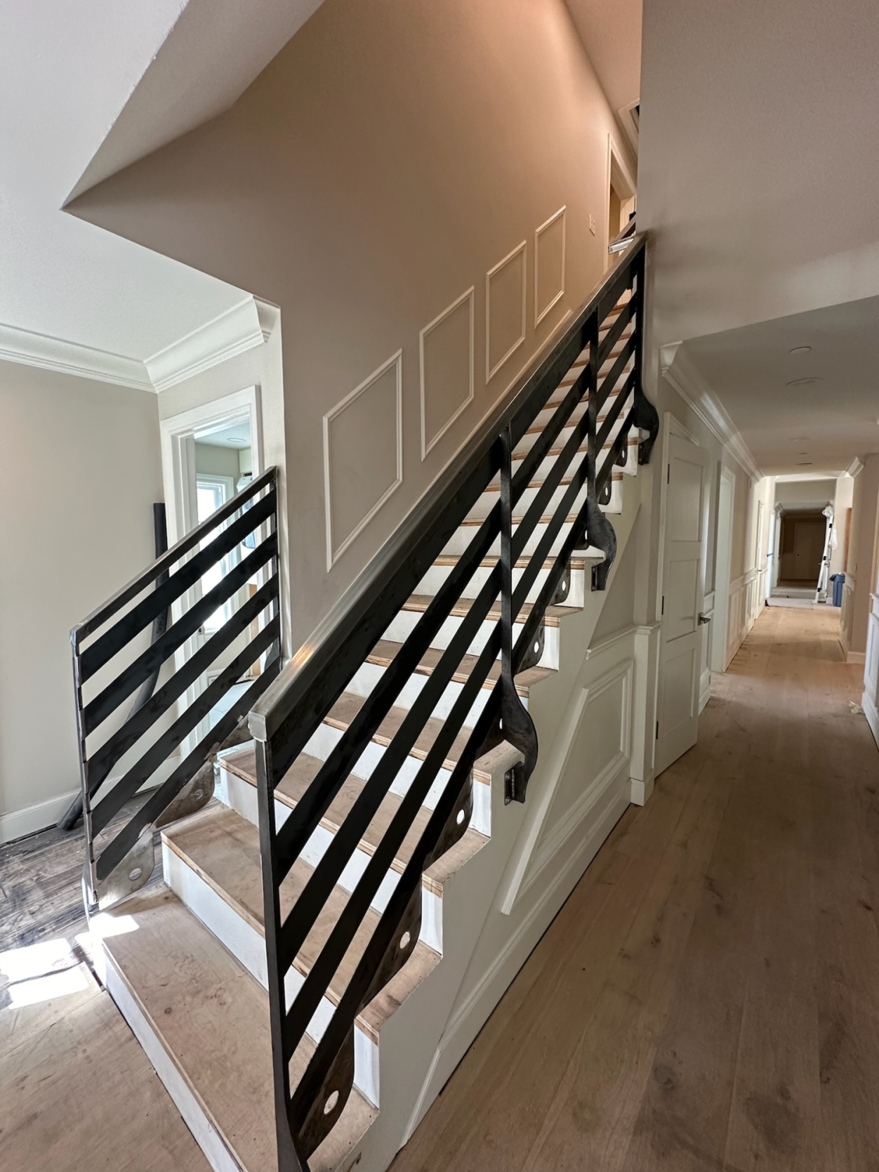 Staircase with black railing leading up to a brightly lit hallway.