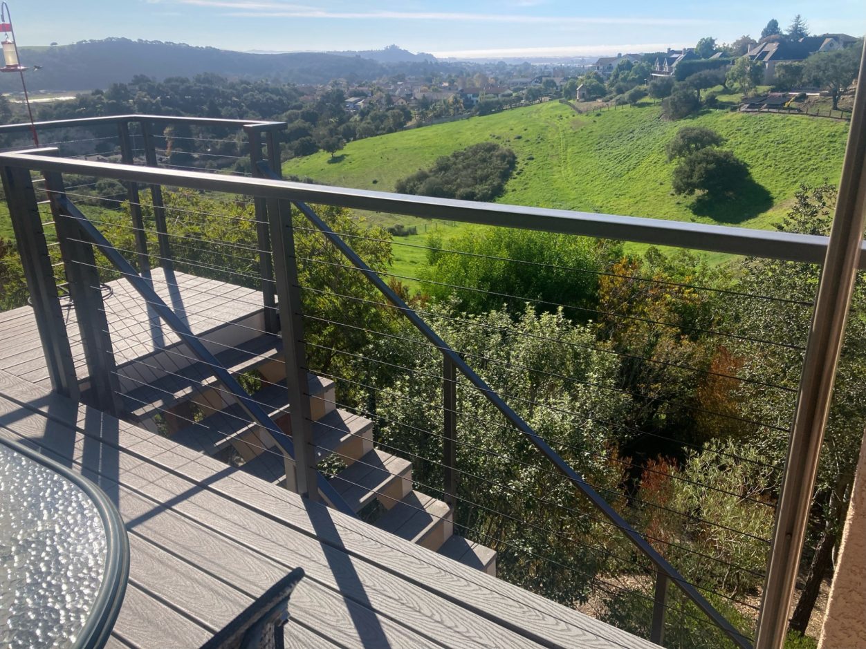 View from a wooden deck overlooking green hills and distant mountains under a clear sky.