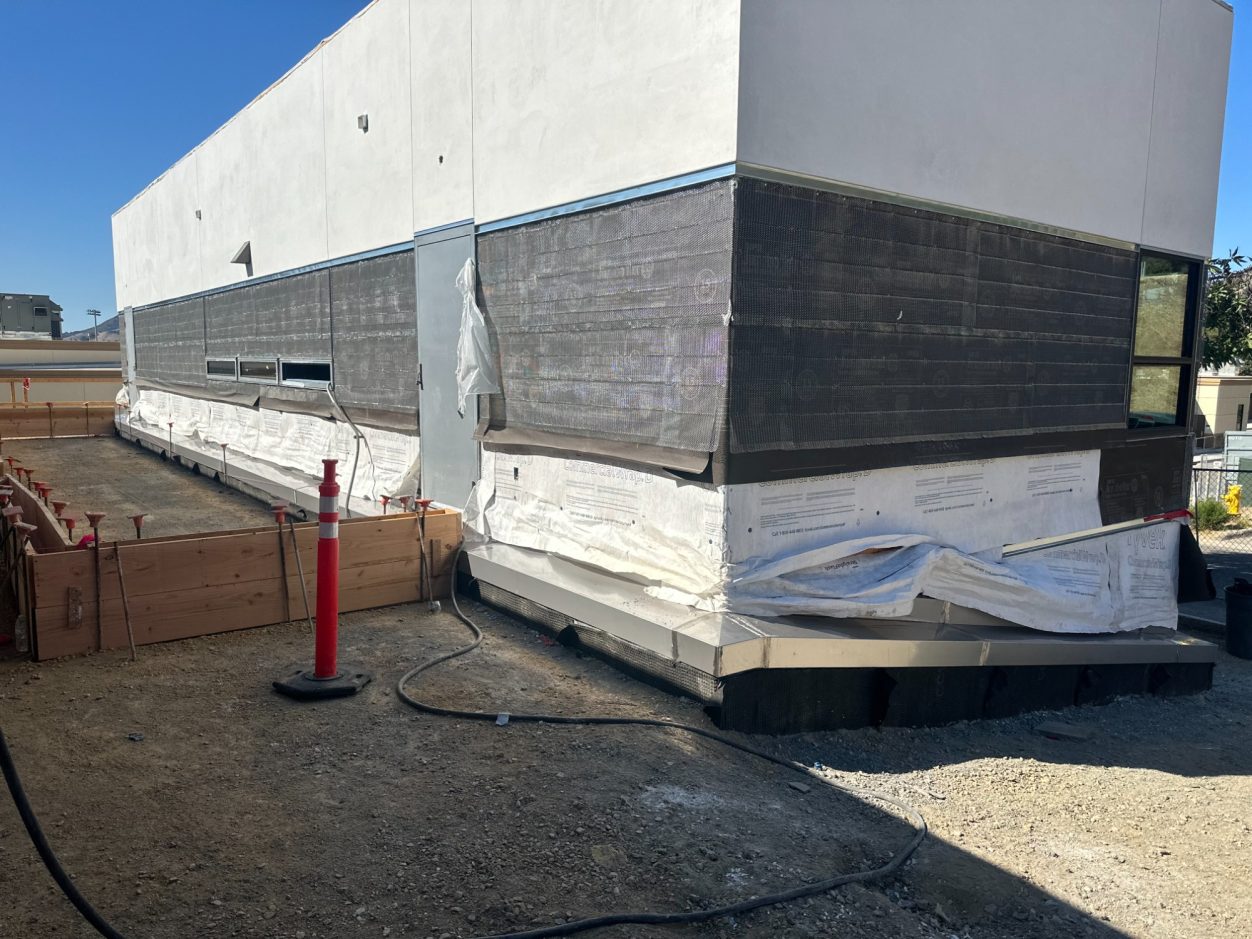 Stainless Steel custom Curb flashing Construction site showing the side of a building with wrapped materials and a red safety cone.