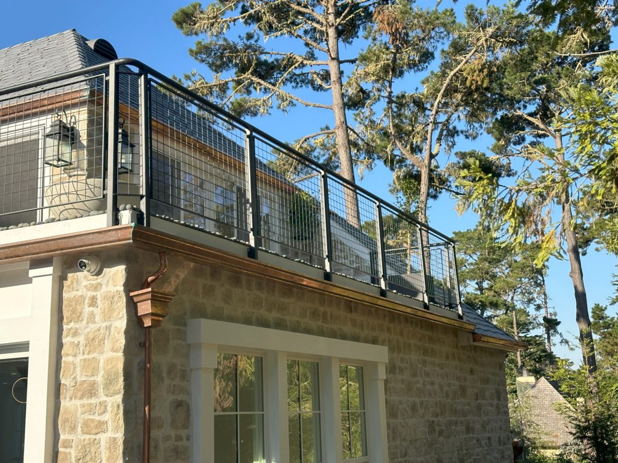 Stone building with a balcony and trees in the background under a clear blue sky.